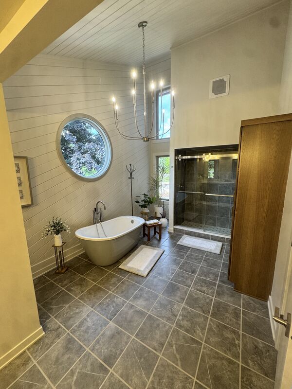Master bathroom with freestanding soaking tub, round window and tile floor