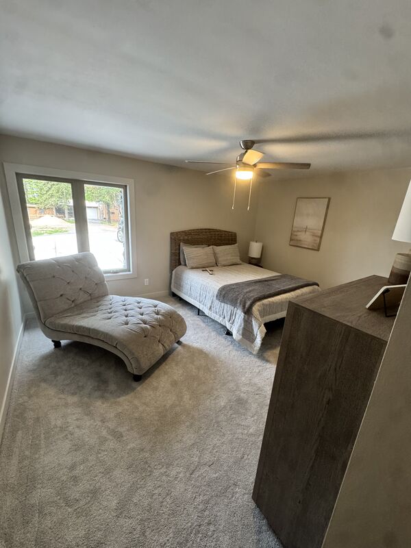 Carpeted bedroom suite with a chaise lounge and natural light