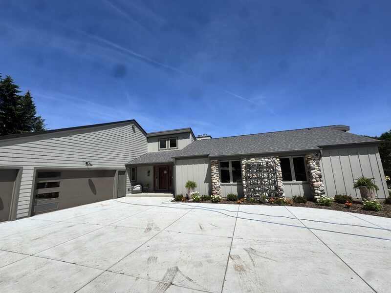 Ranch-style custom home with river-rock stone pillars, board-and-batten siding and a modern glass garage door