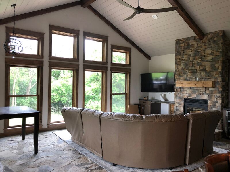 Vaulted great room with timber beams, wall of windows and stone fireplace