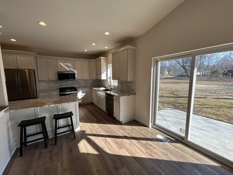 Sunlit kitchen with white cabinets, island seating and sliding patio door