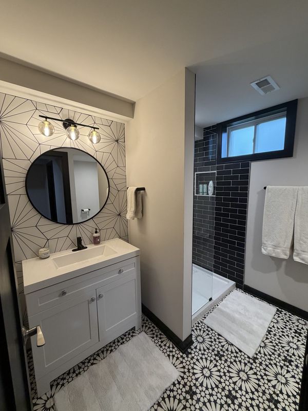 Designer bath with geometric tile accent wall, round mirror and patterned floor