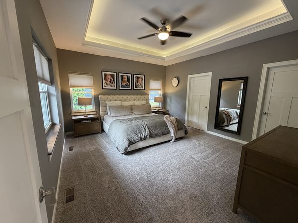 Master bedroom suite with tray ceiling, ceiling fan and staged furnishings