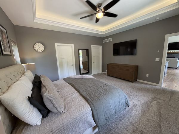Master bedroom with tray ceiling, mounted TV and neutral finishes