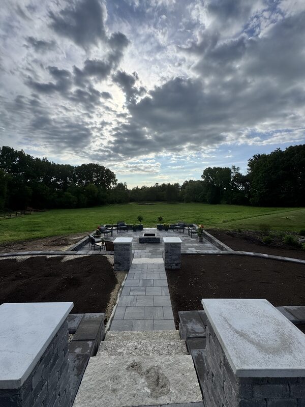 Paver walkway leading between stone pillars to a fire-feature patio at dusk